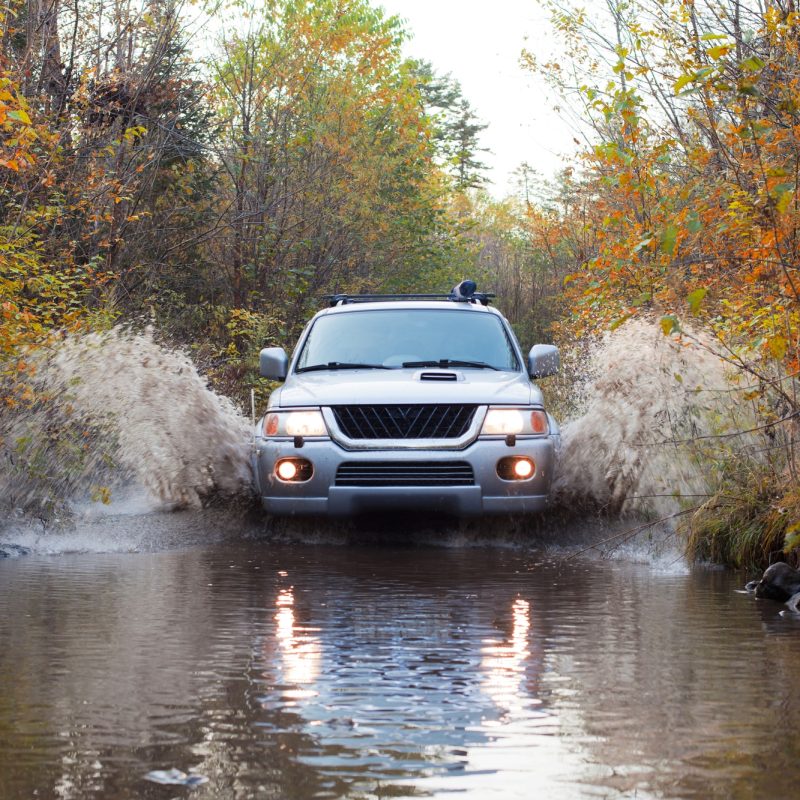 off road truck driving through a large pool of water in the woods